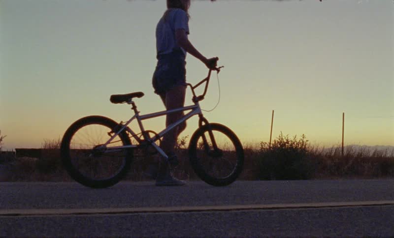 A woman walking a bike down the road