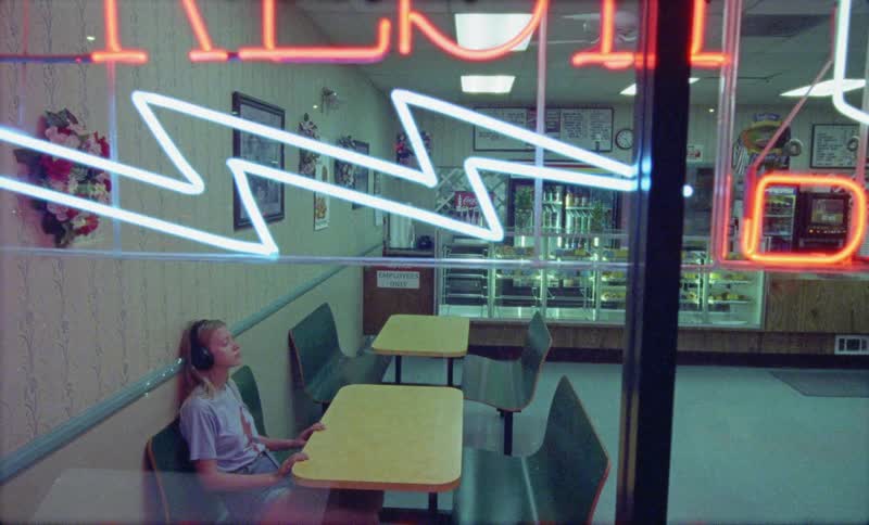 A young woman wearing headphones walking to and sitting at table in a small diner