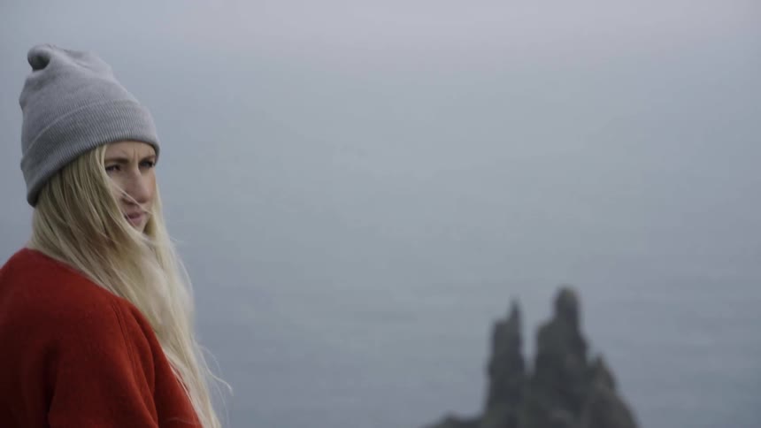 A woman stands near a body of water looking off into the distance