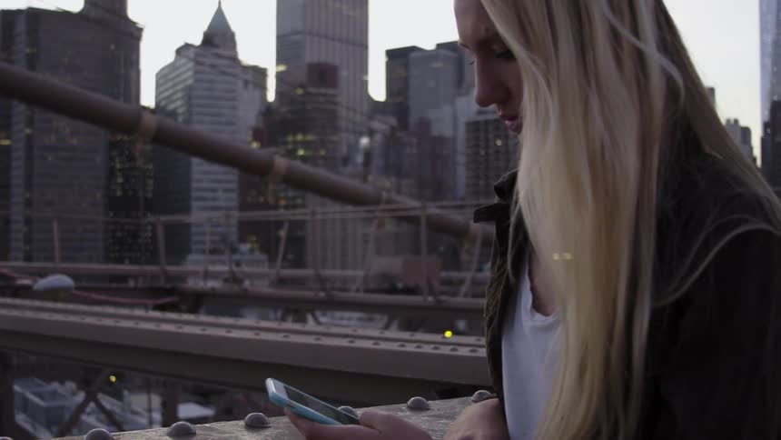 A blond woman plays on her phone on a bridge