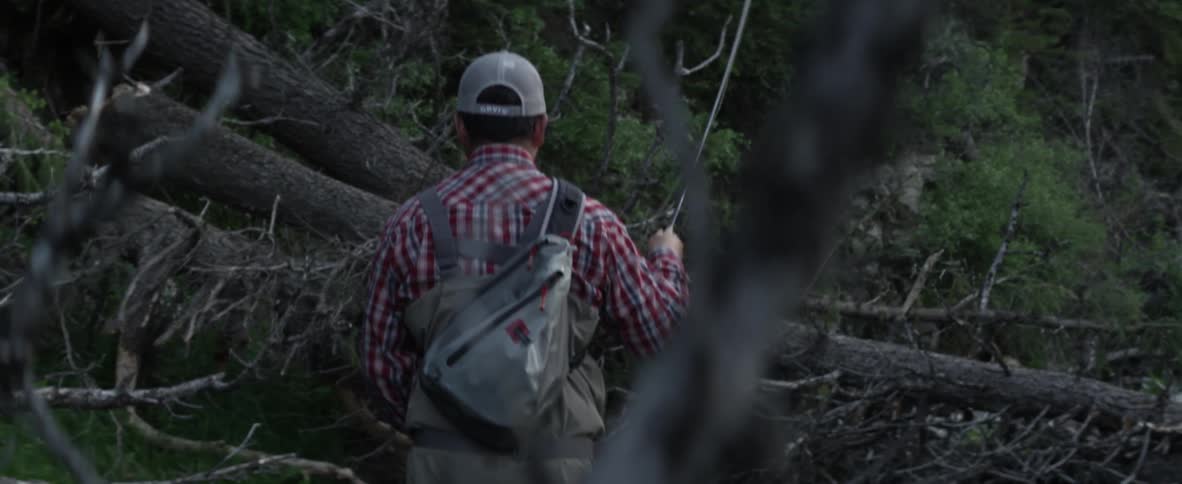 A man is fly fishing by some trees