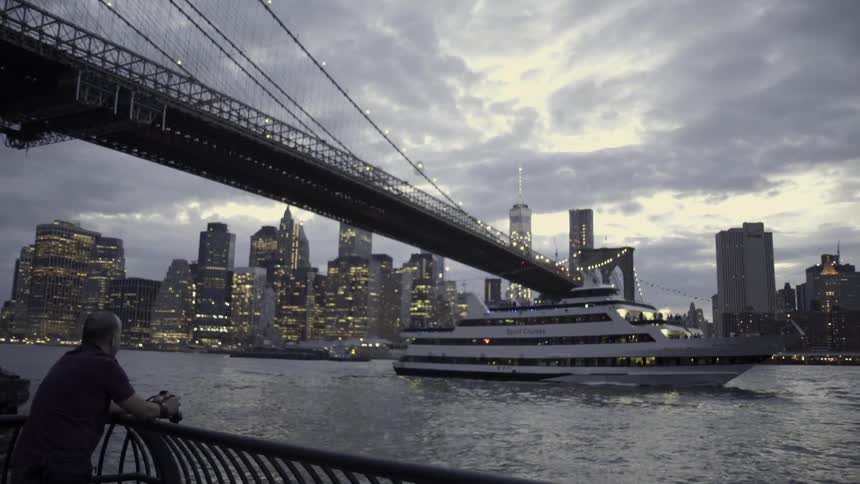A large ship is traveling under a bridge by a city