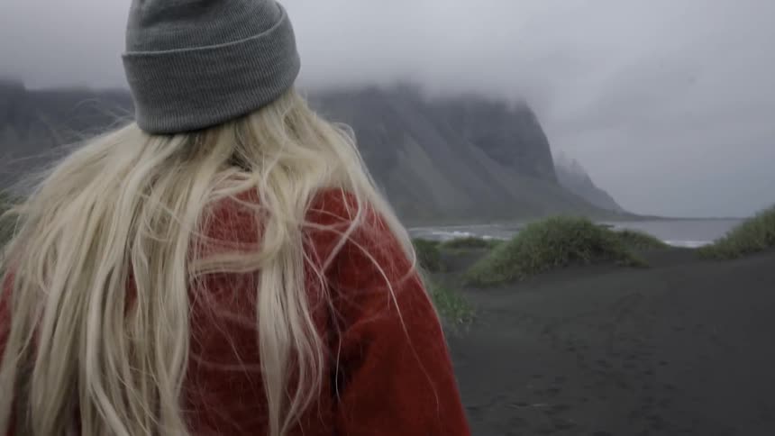 A lady with blonde hair is walking towards the coast on a foggy day