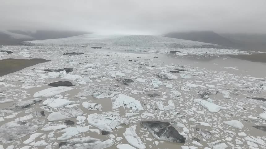 Footage of broken up ice flow and cloud-covered mountains on a dreary day