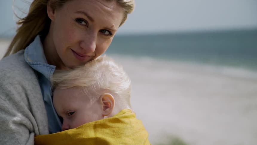 Mother holds and nuzzles toddler while standing on a windy beach