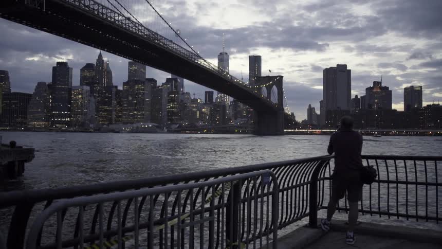 Man leans against a railing overlooking a river flowing beneath a city bridge