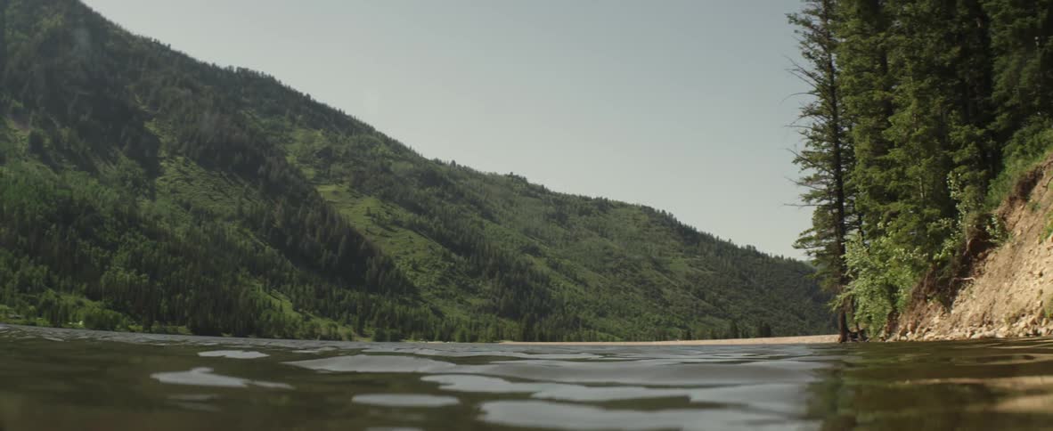 A person jumps into a wide river surrounded by mountains