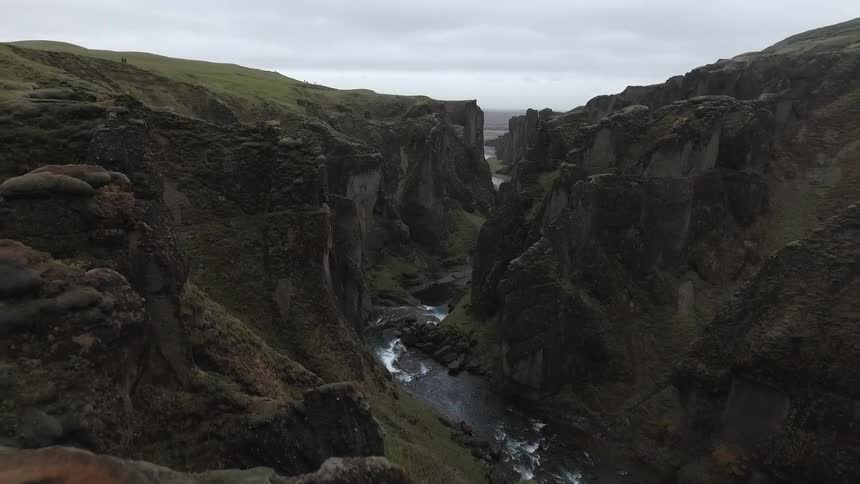 Aerial view of a woman standing on a steep mountain cliff looking out over steep canyon walls and a winding river