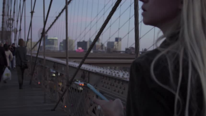 A woman holding a cell phone walks across a pedestrian bridge