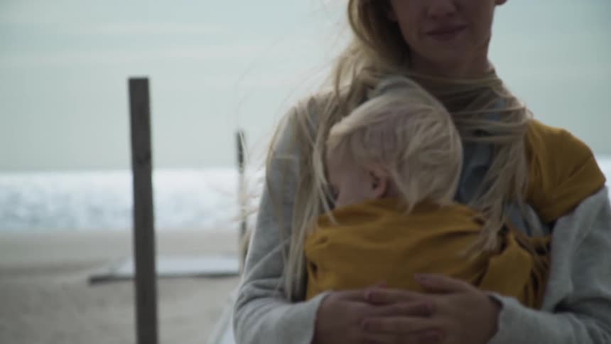 A woman holding a baby is walking away from the beach