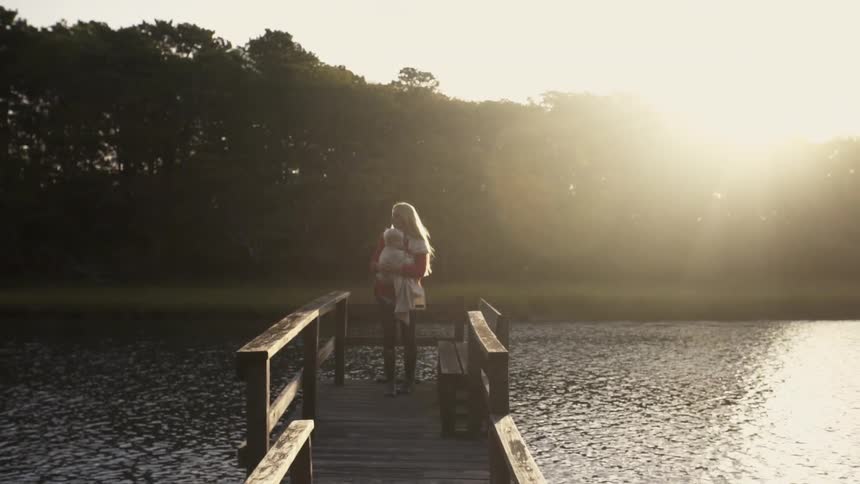A woman holds a baby on a dock on a sunny day