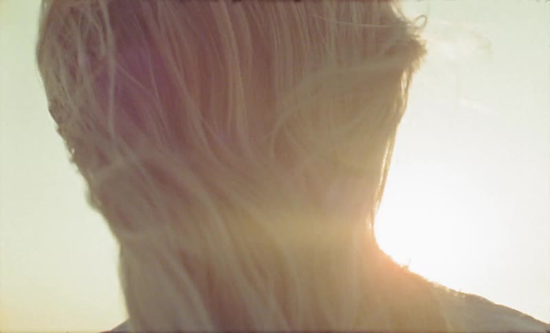 Blonde woman looks at the sun on a windy hair