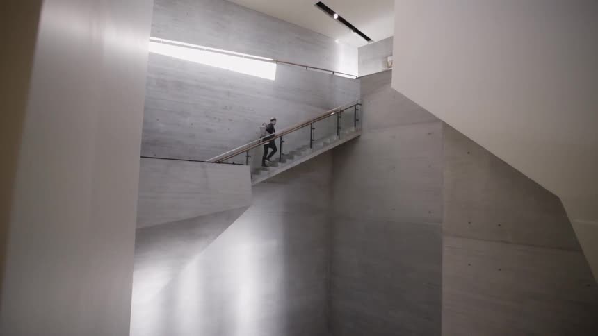 Someone climbs a staircase inside a building with brushed steel walls