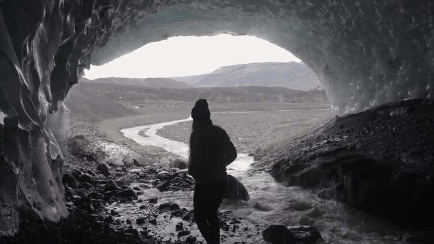 A man walks by a stream under a cave on a cloudy day