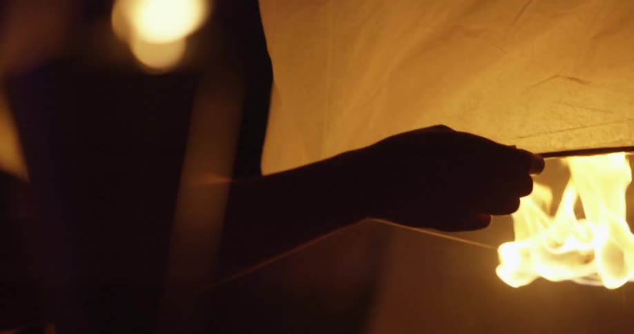 A person holds a paper lantern over a flame