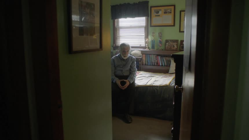 Senior bearded man sits on the bed and thinks in a room
