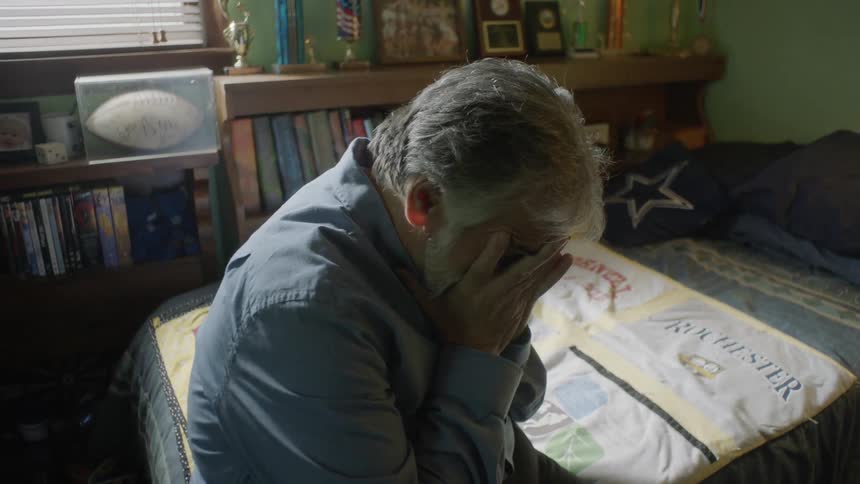 Man sits on edge of bed crying
