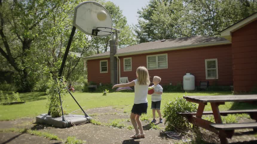 Little girl and boy play basketball in the garden during daylight