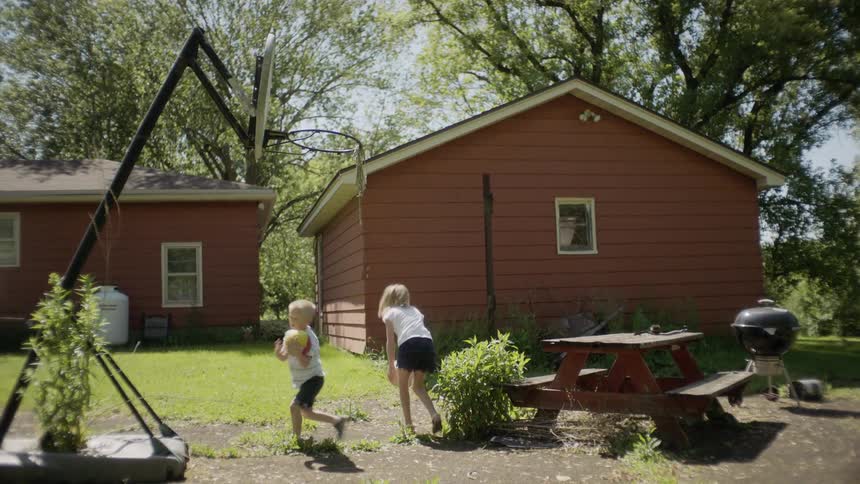 A girl and a boy throwing balls into a basketball hoop in the backyard of a house