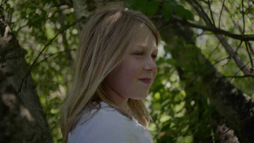 Blonde girl sits in the tree and smiles during the day