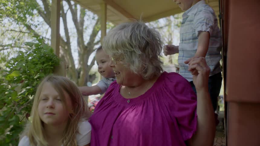 Three children are playing with their grandma on the front porch of a house