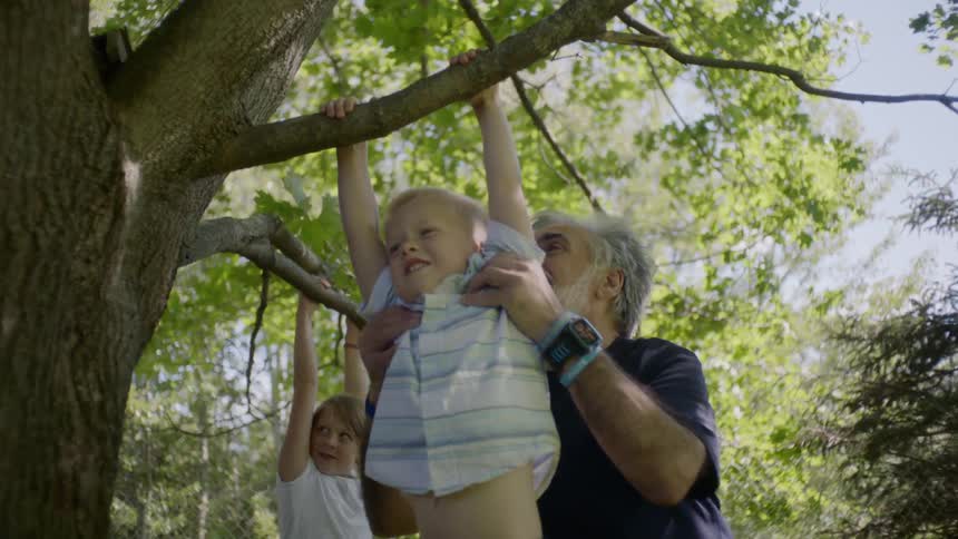 A grandpa plays with his grandchildren in a tree filled yard