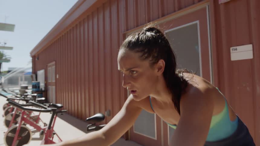 A brunette white woman rides an outdoor stationary bike