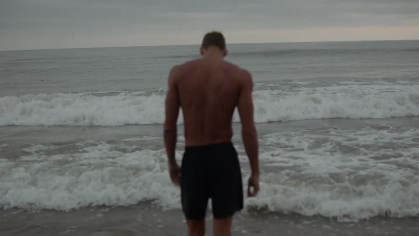 A young man stands on the beach and watches the waves come in