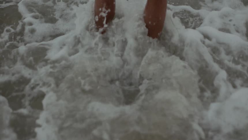 A man is standing on the beach as a small wave washes up around his lower legs