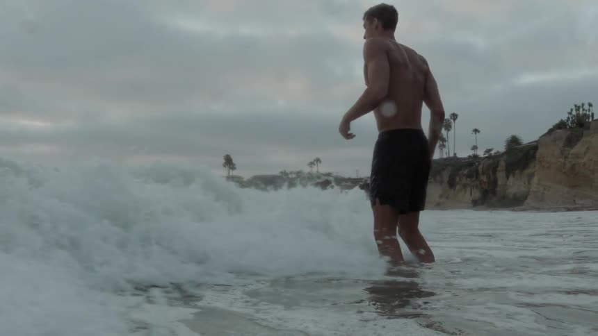 A man standing on the beach getting wet by waves