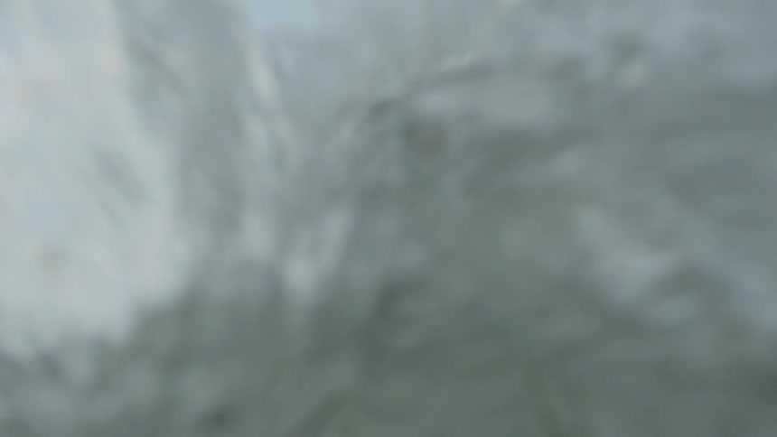 A young man stands on the shore as water comes splashing towards him