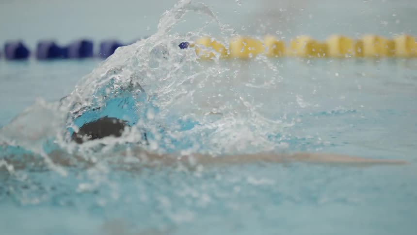 A white male is swimming through blue and yellow racing lanes in a pool