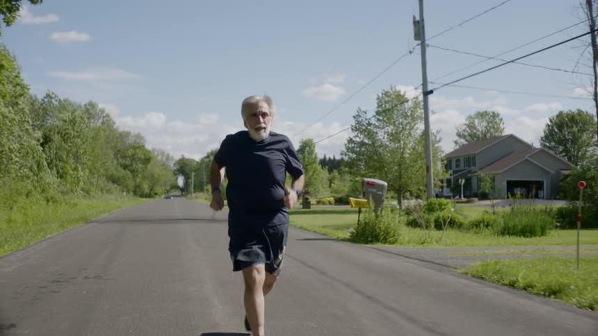 Senior bearded man runs on the road during daylight