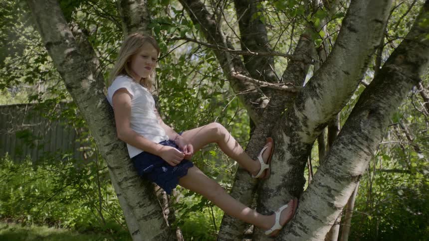 A young girl sits perched in a tree she climbed