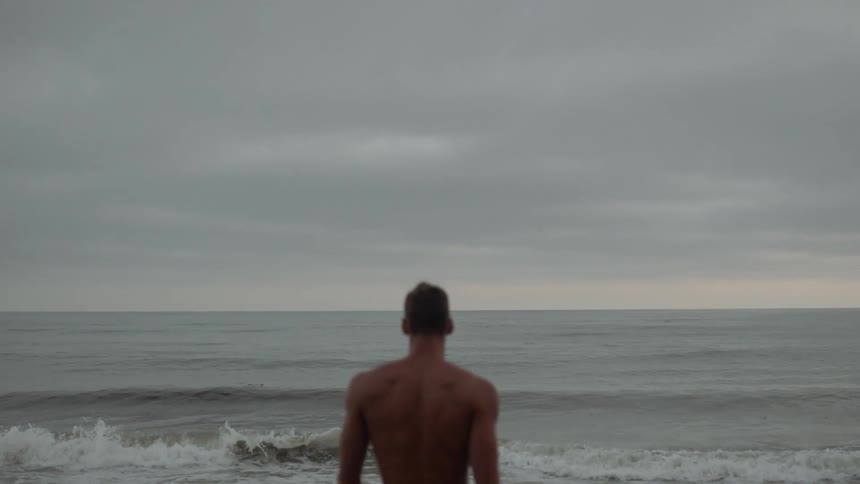 A shirtless male walking toward the beach