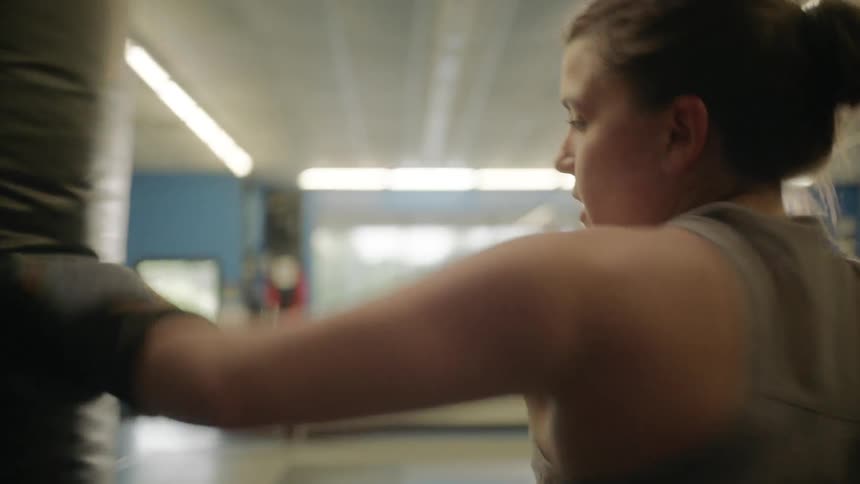 Female boxer wearing boxing gloves hits a punching bag in the gym
