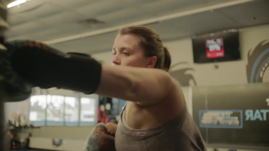 A woman swings widely punching the heavy bag