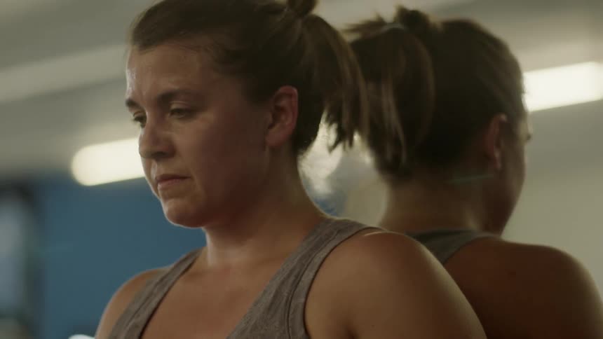 Sweaty woman leans against mirror and breathes in a gym