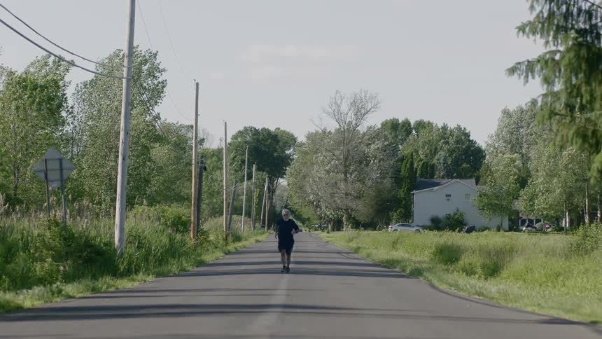 An elder man jogging down the road during the day