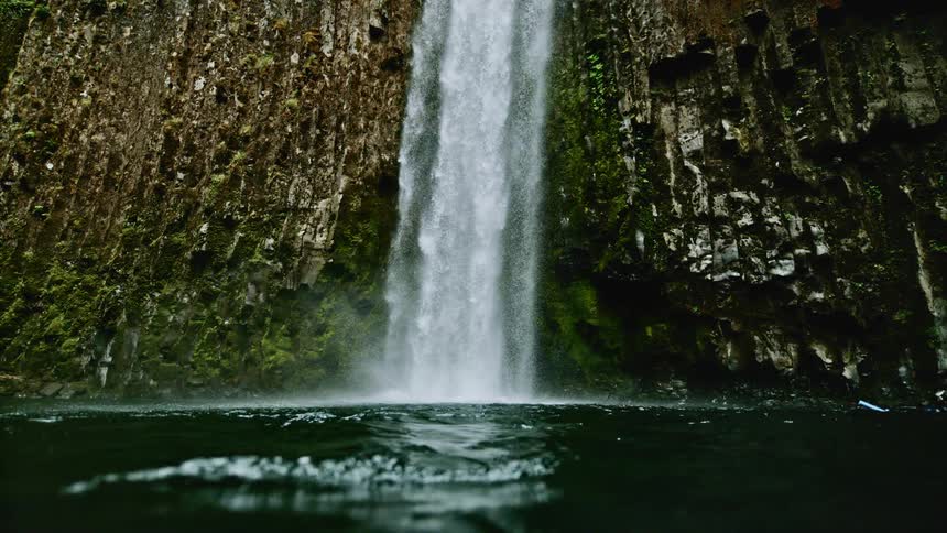 A waterfall into a lake surrounded by moss covered rocks