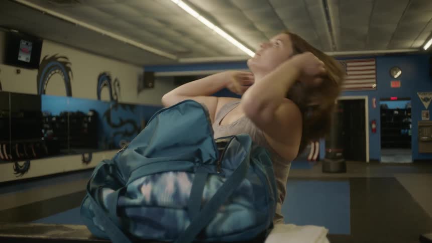 A woman pulls a hair band out of a bag set on the table and puts hair into a ponytail