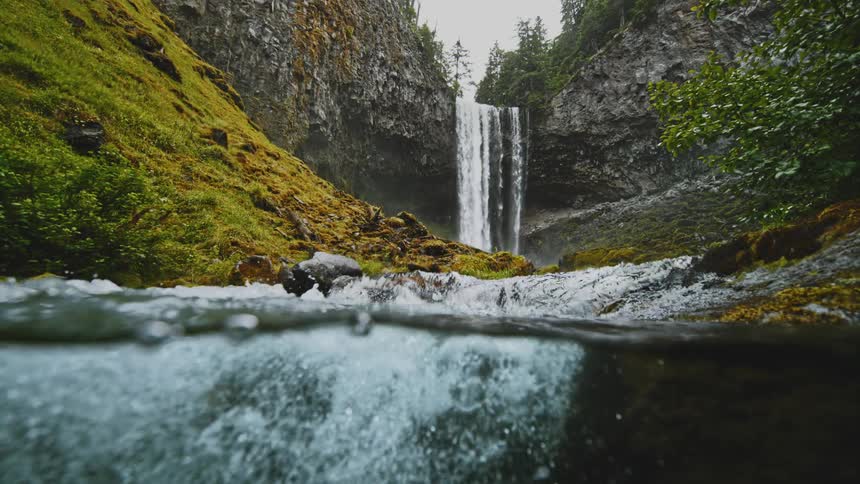 A waterfall spilling into a river that runs down a slope in a valley