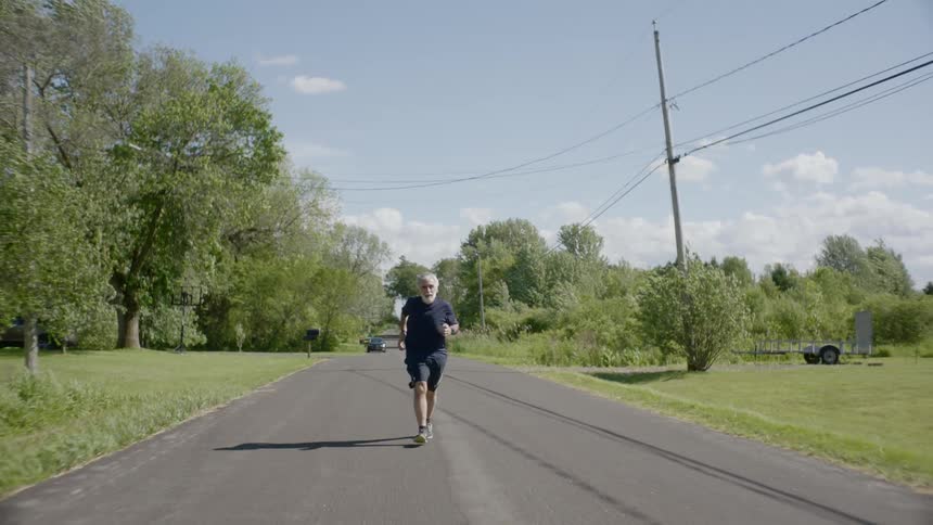 Senior man runs on the asphalt road during dayligh