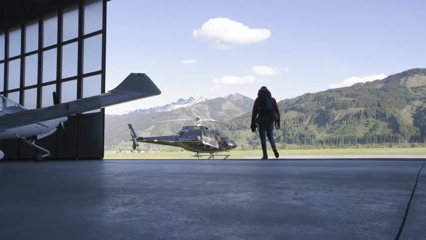 A man walks towards a helicopter thats sitting outside a hanger