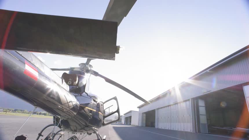 Helicopter with door open sitting on tarmac near a hangar