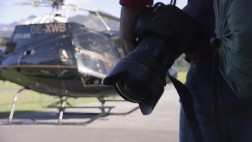 A man carrying a camera walks to a helicopter