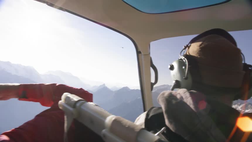 Three people ride a helicopter over the mountains