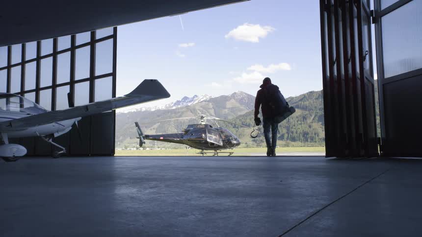 A man is walking out of the hangar towards the helicopter