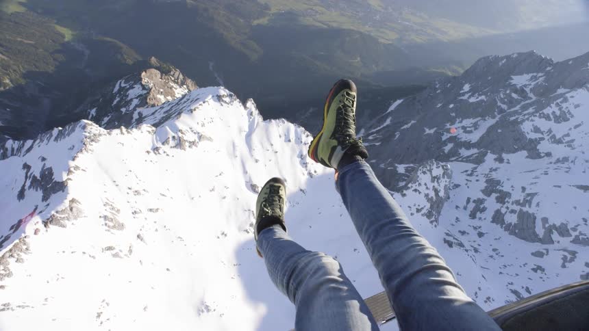 A person stretches their legs out while riding in the air above a mountain