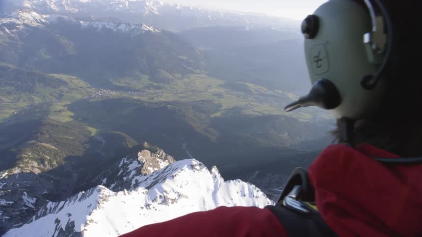 A man dangles his legs outside of a flying helicopter